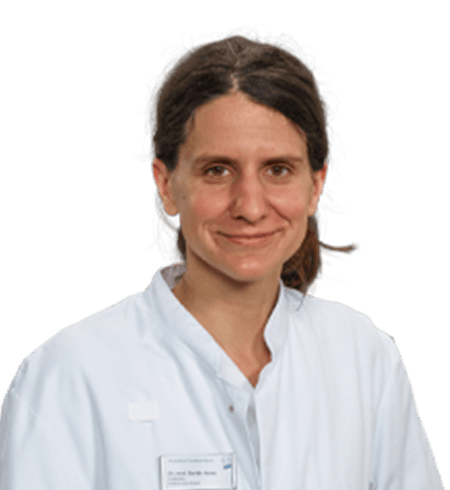 Eine Person mit langen braunen Haaren trägt einen weißen Laborkittel über einem hellen Hemd und blickt mit neutralem Gesichtsausdruck in die Kamera. Der Hintergrund ist transparent.